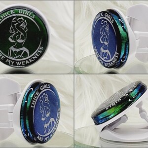 May include: A white phone grip with a round, blue and green iridescent design. The design features a silhouette of a woman with the text "THICK GIRLS ARE MY WEAKNESS".