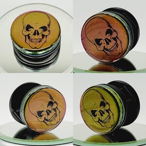 May include: A set of four black and iridescent skull ear gauges. The gauges are made of acrylic and feature a skull design with a black outline. The gauges are available in a variety of sizes.