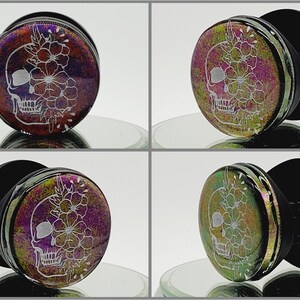 May include: A pair of black and iridescent ear gauges featuring a white skull and floral design. The gauges are shown from different angles.