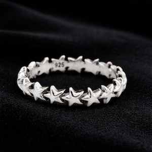 Könnte beinhalten: Ein silberfarbener Ring mit einem durchgehenden Band aus kleinen, miteinander verbundenen Sternformen. Die Innenseite des Rings ist deutlich mit der Zahl 925 geprägt, was die Metallzusammensetzung angibt. Der Ring hat eine polierte Oberfläche.