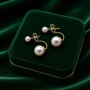 May include: A pair of gold-tone earrings featuring a double-sided design with a smaller white pearl stud at the front and a larger white pearl suspended on a curved gold-tone bar that extends behind the earlobe, creating a layered appearance.