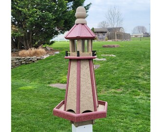 May include: A red and brown wooden bird feeder shaped like a lighthouse with a white post. The feeder has a hexagonal base and a pointed roof with a small white finial.