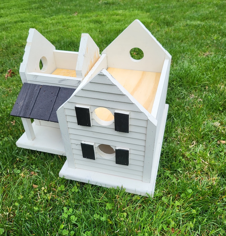 May include: A white wooden birdhouse with a black roof and black accents. The birdhouse has a small porch and multiple round openings.