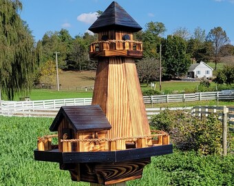 May include: A wooden birdhouse shaped like a lighthouse with a black roof and a small birdhouse attached to the side. The birdhouse is mounted on a wooden pole and is surrounded by green grass.