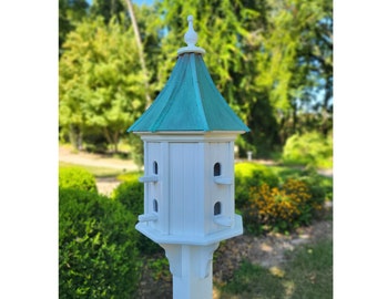 Puede incluir: Una casita de pájaros blanca con un techo verde y un poste blanco. La casita de pájaros tiene tres compartimentos de anidación y un remate decorativo en la parte superior.