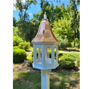 May include: White bird feeder with a copper roof and a decorative finial. The feeder has a hexagonal base and four sides with openings for birds to access the food.