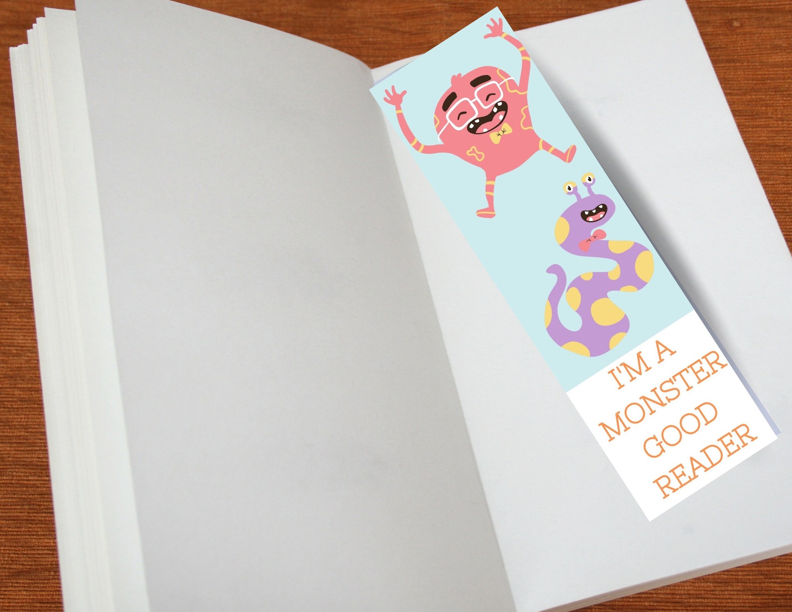 An open notebook with a blue bookmark featuring colourful monsters. At the bottom in orange against a white background it reads: "I'm a monster good reader" 