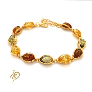 May include: A gold bracelet with a series of teardrop-shaped amber stones in shades of yellow, brown, and green. The bracelet has a delicate chain and clasp. The amber stones are connected by gold links.