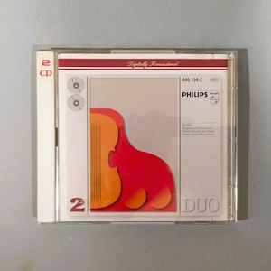 Puede incluir: Un set de 2 CD Philips DUO en una caja de plástico transparente. La portada presenta una forma de violín naranja estilizada sobre un fondo rojo. El texto "Digitally Remastered" y "PHILIPS" son visibles.