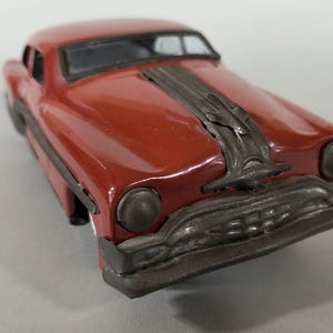 Peut inclure: Une voiture miniature en métal moulé sous pression de couleur rouge foncé. Le véhicule présente un pare-chocs avant en métal gris foncé, des phares circulaires assortis et un ornement de capot gris foncé distinctif vers le pare-brise.