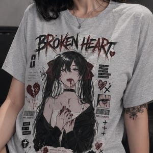 May include: A heather gray short-sleeve t-shirt featuring a graphic print of an anime-style character with long dark hair, red ribbons, and blood on their face and hands. The text BROKEN HEART appears at the top with additional small text.