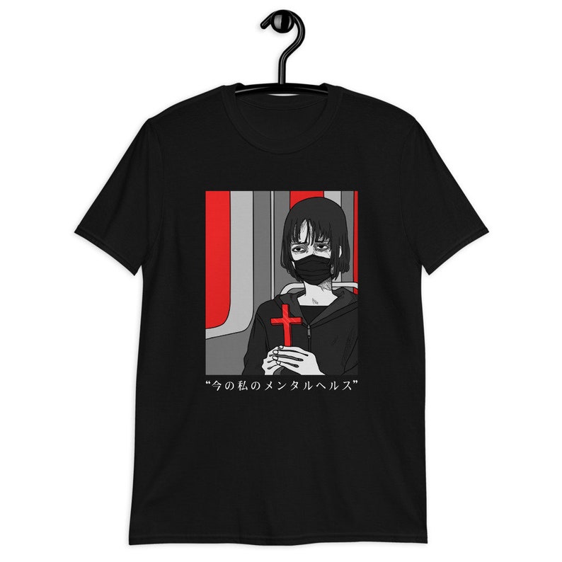 May include: A black short-sleeve t-shirt featuring a graphic print of a person with short dark hair wearing a black face mask. The person holds a bright red cross. The background is red and gray. Below the image is the text &ldquo;今の私のメンタルヘルス&rdquo;.