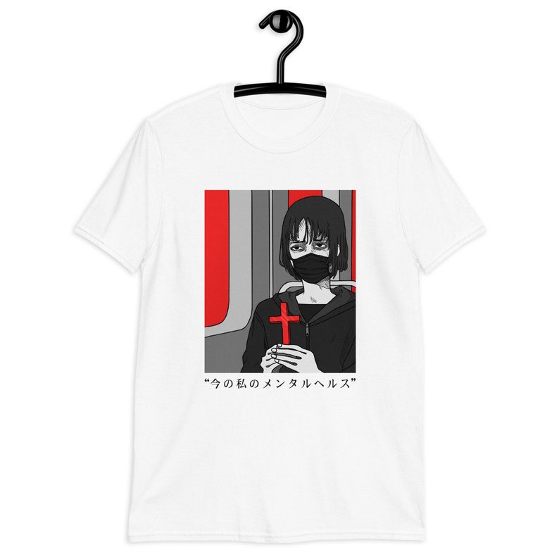 May include: A white short-sleeve t-shirt featuring a graphic print of a person with short black hair wearing a black face mask and a black hoodie. The person holds a red cross. The background is red and gray. Text reads: 今の私のメンタルヘルス.