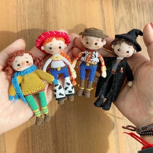 May include: Four crocheted dolls, each with a different character design. The dolls are wearing colorful outfits and hats. The dolls are sitting on a person's hands.