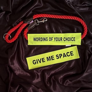 May include: A red rope dog lead with a metal clasp and two yellow rectangular patches. One patch reads "WORDING OF YOUR CHOICE" and the other reads "GIVE ME SPACE" in black capital letters. The background is a dark, shiny fabric.