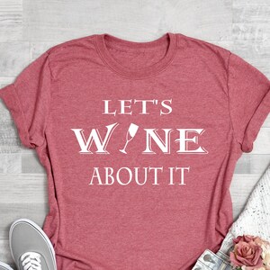 May include: Red t-shirt with white text that reads "Let's Wine About It". The text includes a wine glass graphic.