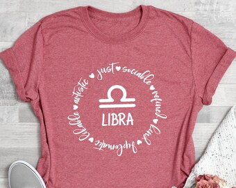 May include: Coral pink t-shirt with a white circle graphic featuring the Libra zodiac symbol and the words "just", "sociable", "refined", "artistic", "charitable", "fair", "harmonious", and "Libra".