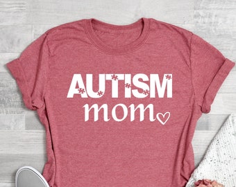 May include: Coral pink t-shirt with the text "AUTISM mom" in white with a small white heart after the word "mom".