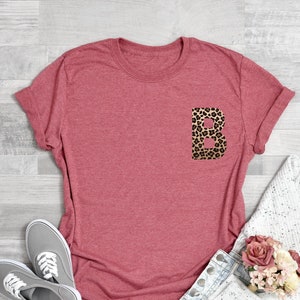 May include: Coral pink t-shirt with a leopard print letter "B" on the front pocket.