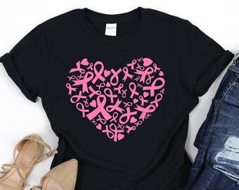 Puede incluir: Camiseta negra con un diseño de corazón rosa hecho de cintas rosas. El corazón está centrado en la camiseta. La camiseta está puesta plana sobre una superficie blanca.