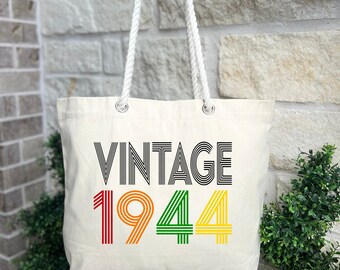 May include: A white canvas tote bag with rope handles. The bag has a black and white striped design that says "Vintage 1944" in colorful stripes.