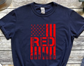 May include: Navy blue t-shirt with a distressed red American flag design and the words "REMEMBER EVERYONE DEPLOYED RED". The graphic includes soldier silhouettes. The shirt is shown with denim jeans and a straw hat.