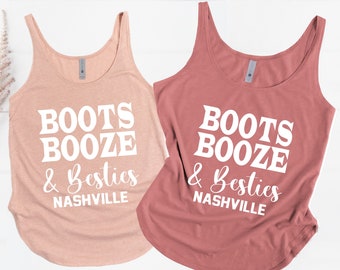 May include: Two tank tops with the text "Boots Booze & Besties Nashville" in white. The tank top on the left is a light pink color and the tank top on the right is a darker pink color.