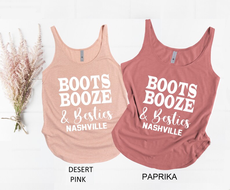 May include: Two tank tops with the text "Boots Booze & Besties Nashville" in white. The tank top on the left is a light pink color and the tank top on the right is a darker pink color.