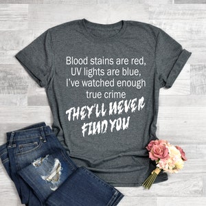 May include: Gray t-shirt with white text that reads "Blood stains are red, UV lights are blue, I've watched enough true crime THEY'LL NEVER FIND YOU".