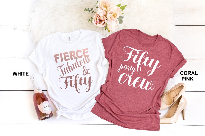 May include: Two t-shirts with a 50th birthday theme. One white t-shirt says "Fierce Fabulous & Fifty" in rose gold lettering. The other coral pink t-shirt says "Fifty party crew" in white lettering.