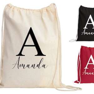 May include: Three drawstring bags with the letter "A" and the name "Amanda" printed on them. The bags are in three different colors: natural, black, and red.
