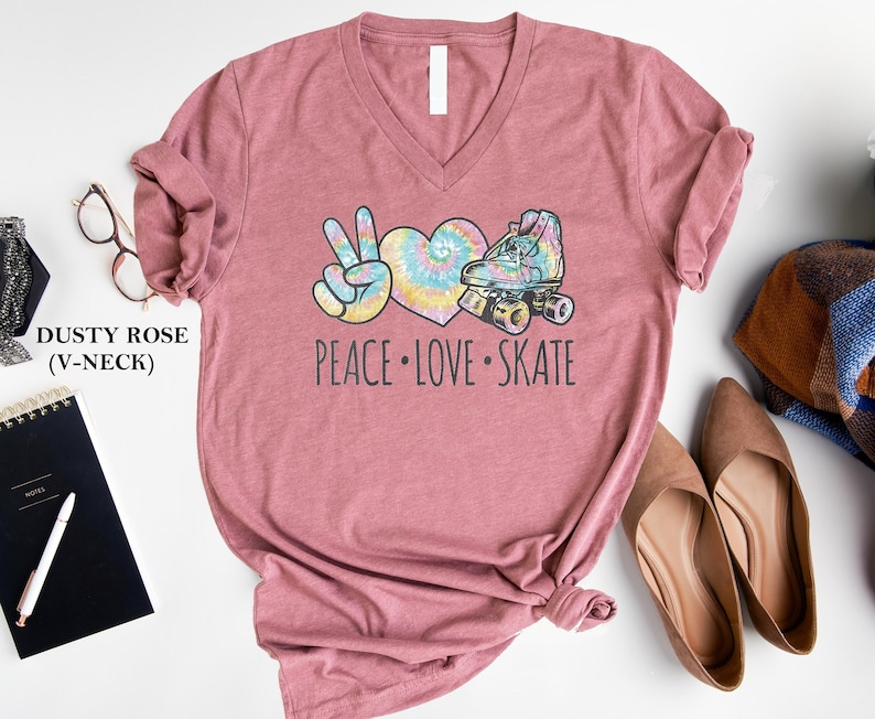 May include: Dusty rose V-neck t-shirt with a tie-dye heart, peace sign, and roller skate graphic. The text "Peace Love Skate" is printed below the graphic.