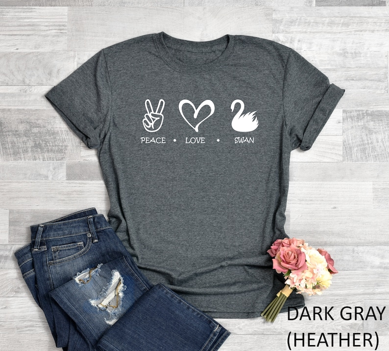 Puede incluir: Camiseta gris oscuro jaspeada con un gr&aacute;fico blanco de signo de paz, coraz&oacute;n y cisne. El texto "Peace Love Swan" est&aacute; impreso debajo del gr&aacute;fico.