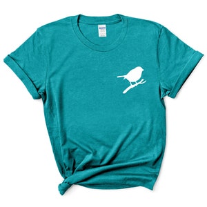 May include: Teal blue t-shirt with a white silhouette of a bird on a branch.