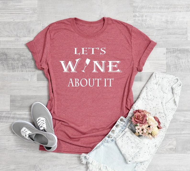 May include: Red t-shirt with white text that reads "Let's Wine About It". The text includes a wine glass graphic.