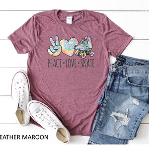 May include: Heather maroon t-shirt with a peace sign, heart, and roller skate graphic. The graphic is in tie-dye colors. The text "Peace Love Skate" is printed below the graphic.