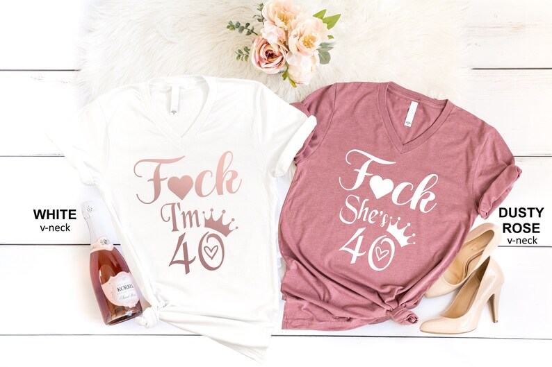 May include: Two v-neck t-shirts with the text "Fock I'm 40" and "Fock She's 40" in rose gold lettering with a heart and crown graphic. The shirts are white and dusty rose.