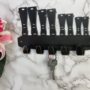 May include: Black metal key holder shaped like a row of boots. There are six hooks on the bottom of the holder.