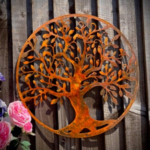 Può includere: Un decoro da parete in metallo color ruggine arancione a forma di albero della vita, con forma circolare e dettagli intricati. L'albero ha un tronco spesso e molti rami con foglie.