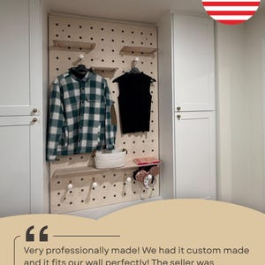 May include: A light-colored wooden pegboard wall organizer featuring multiple circular holes, adjustable shelves, and round pegs. The board displays a green and white plaid shirt, a black sleeveless top, a white woven basket, and a pair of ears.