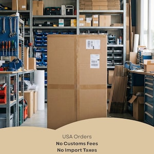 May include: A large, rectangular brown cardboard shipping box stands in the center of a warehouse storage area. The box features two white shipping labels on its front surface. The background shows metal shelving units filled with various boxes and tools.