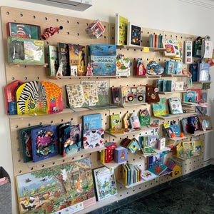 May include: A display of children's books on a wooden pegboard. The books are of various sizes and colors, with illustrations of animals, nature scenes, and other kid-friendly themes. Some books are stacked, while others are displayed upright.