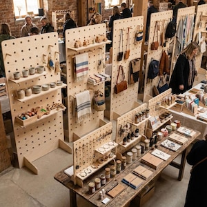 Puede incluir: Un bullicioso mercado artesanal con diversos productos hechos a mano exhibidos en expositores de madera perforada y mesas r&uacute;sticas. Los art&iacute;culos incluyen cer&aacute;mica, joyer&iacute;a, bolsos de cuero y textiles. Los compradores exploran la selecci&oacute;n.
