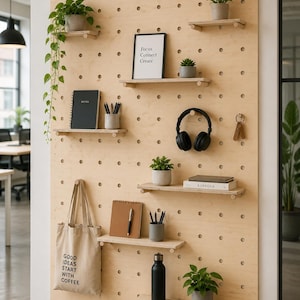 May include: A large light-colored wooden pegboard wall organizer featuring multiple adjustable shelves holding potted plants, a framed sign reading Focus Connect Create, a black notebook, pens, headphones, a tote bag with text, and a water bottle.