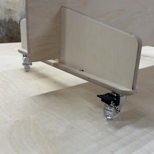 May include: A light-coloured wooden storage unit with a series of evenly spaced, semi-circular cutouts along the top edge. The unit has a side panel with a smaller, angled section and is mounted on clear caster wheels.