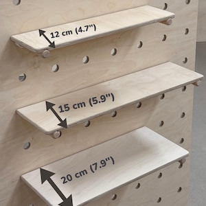 May include: Three wooden shelves of varying sizes, designed for a pegboard system. The shelves are made of light-colored wood and are 4.7", 5.9", and 7.9" (12, 15, and 20 cm) wide, respectively. Each shelf has small wooden pegs for support.