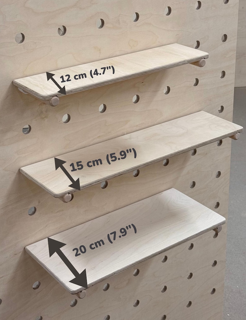 May include: Three wooden shelves of varying sizes, designed for a pegboard system. The shelves are made of light-colored wood and are 4.7", 5.9", and 7.9" (12, 15, and 20 cm) wide, respectively. Each shelf has small wooden pegs for support.