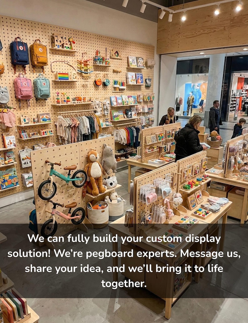 Op de afbeelding: Een winkelinterieur met lichtgekleurde houten pegboard-wanden en vrijstaande displays. De schappen bevatten diverse kinderartikelen, waaronder rugzakken, knuffels, loopfietsen, boeken en kleding aan kledinghangers.
