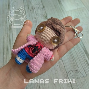 May include: A handmade crochet doll with a brown head, button eyes, and a pink jacket. The doll has a red and black spider design on the chest and blue pants. A silver keychain is attached. The text "LANAS FRIKI" is at the bottom.