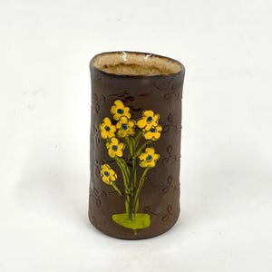 May include: A brown ceramic vase with a textured surface and a hand-painted design of yellow flowers with blue centers.